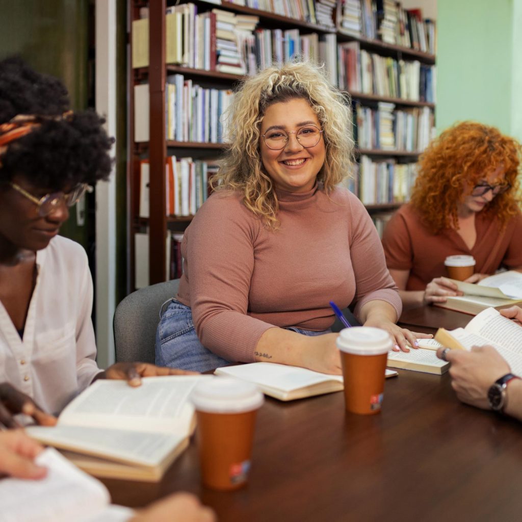 A diverse group of individuals sitting at a table in a library, engrossed in books and studying together.
