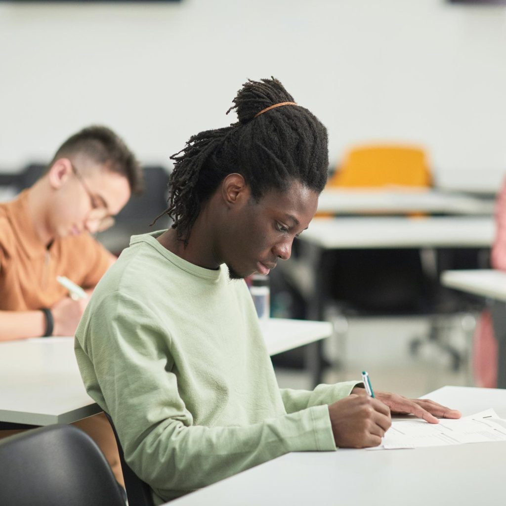 A student is focused on writing on a paper at a desk in a classroom setting.